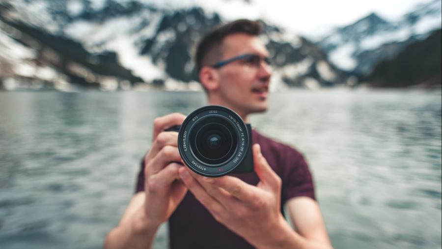 Man staat met een professioneel fototoestel met lens van Carl Zeiss in de bergen